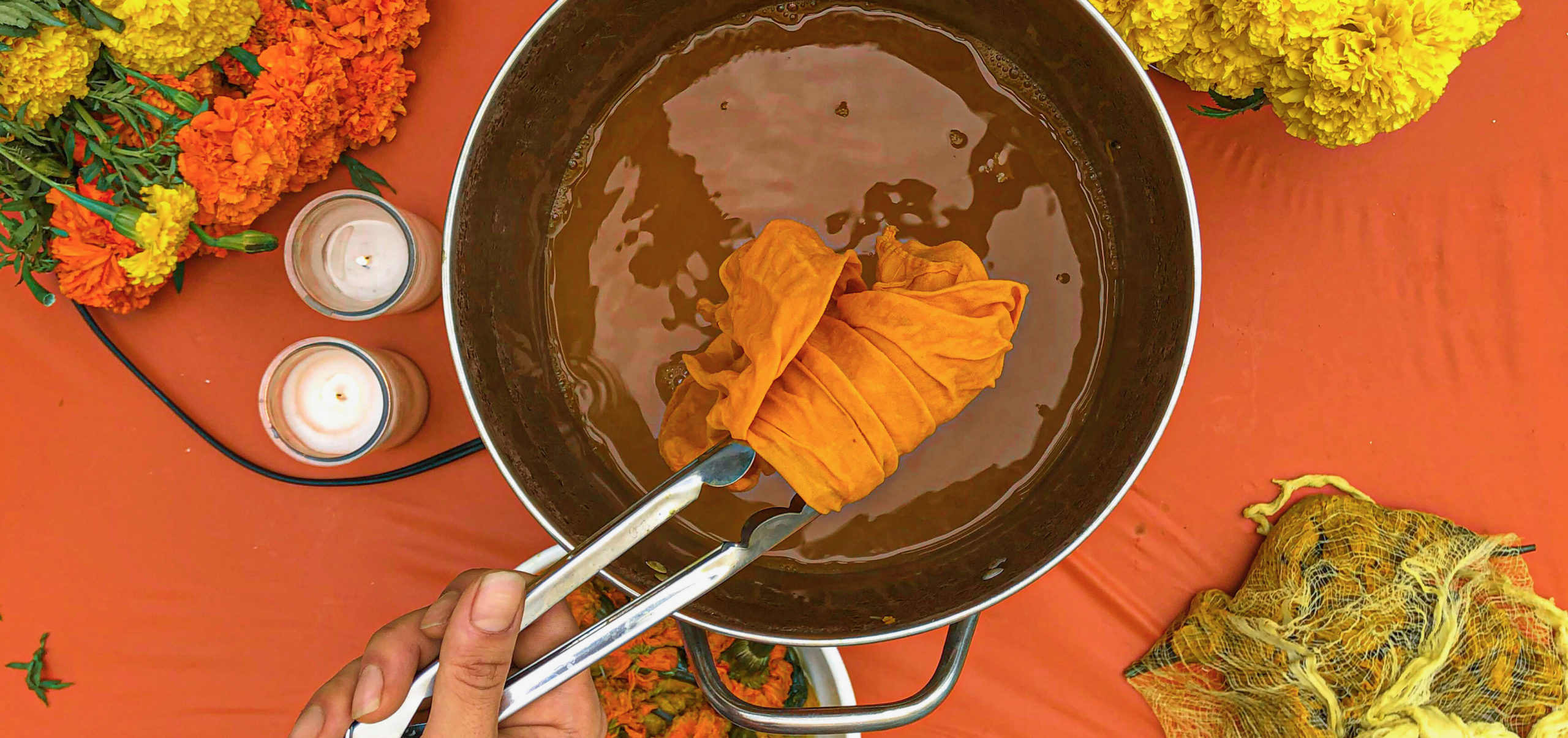 Image of someone dipping fabric into a pot of dye naturally made from marigolds.